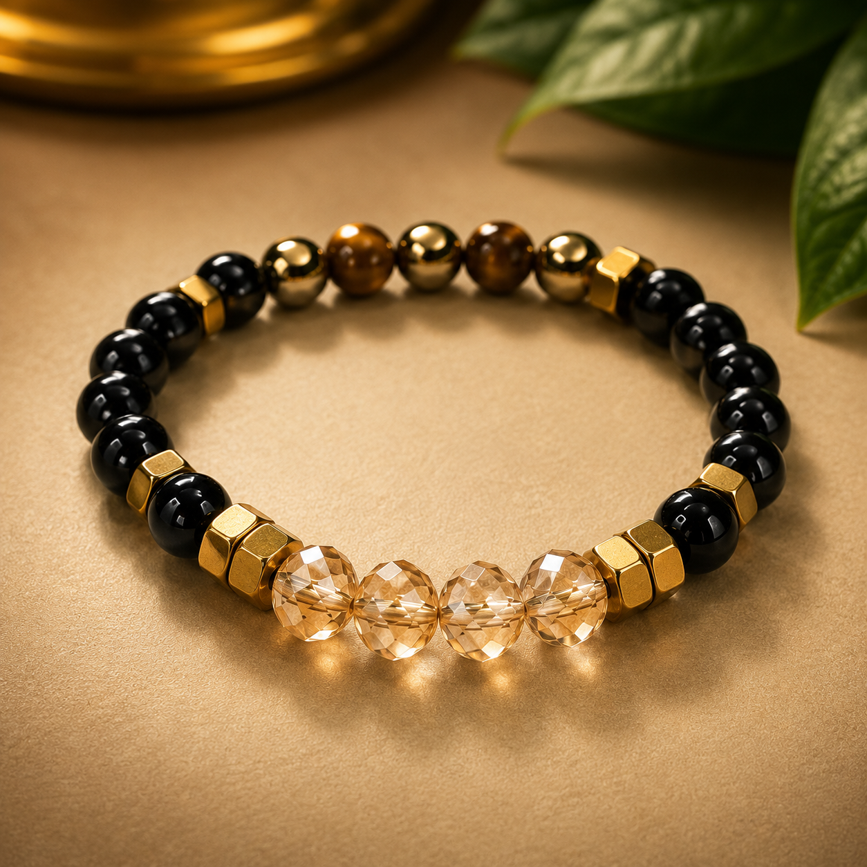 Beaded bracelet with black, gold, and clear beads on a beige surface with green leaves.