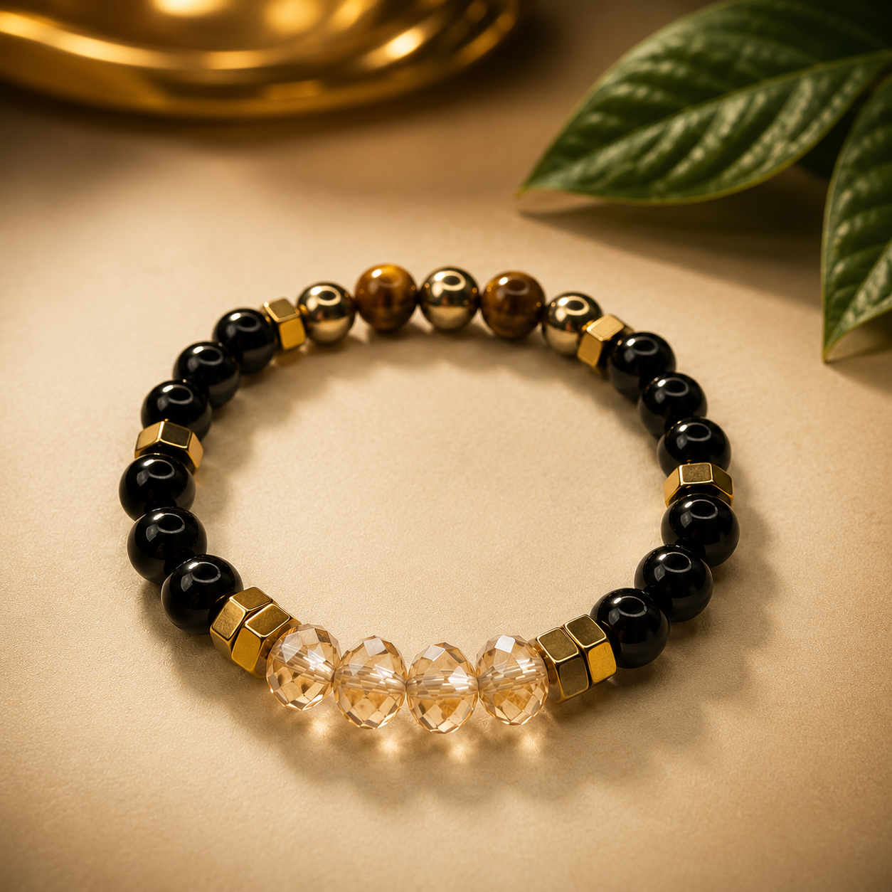 Bracelet with black, gold, and clear beads on a beige surface with a leaf in the background