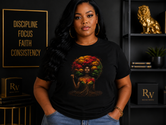 A woman wearing a black graphic t-shirt with a colorful tree design, standing in a styled room with a black background and gold-framed decor.