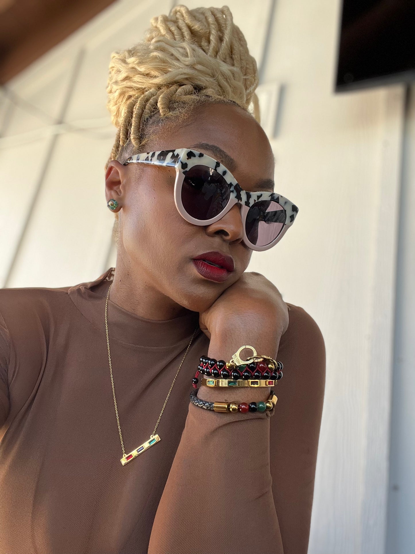 Person wearing leopard print sunglasses, a brown top, and colorful bracelets with a neutral background.
