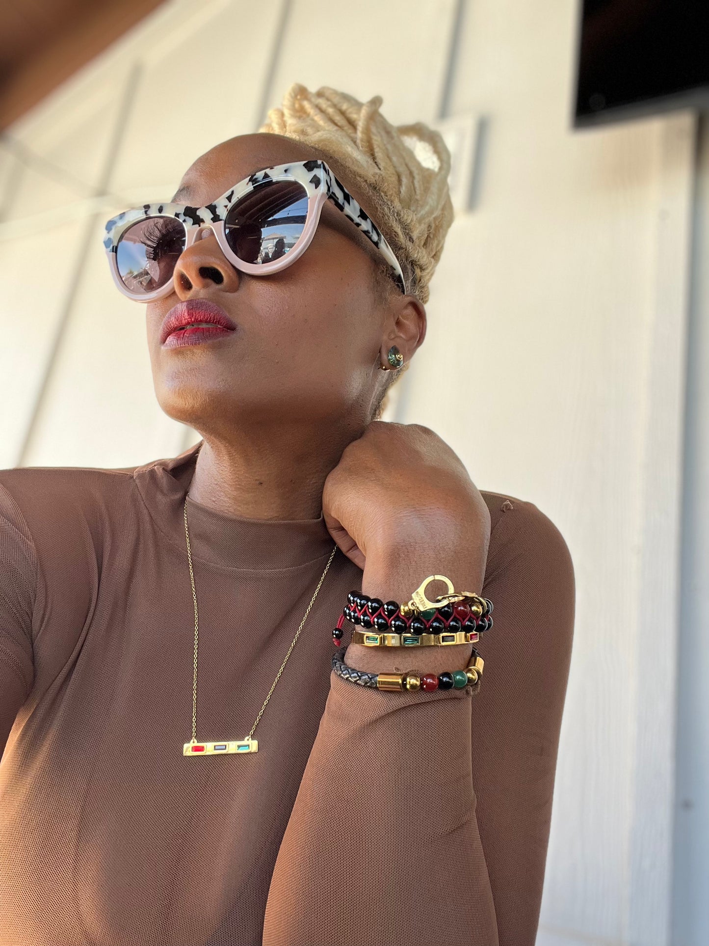 Person wearing sunglasses and a brown top with colorful bracelets on a neutral background
