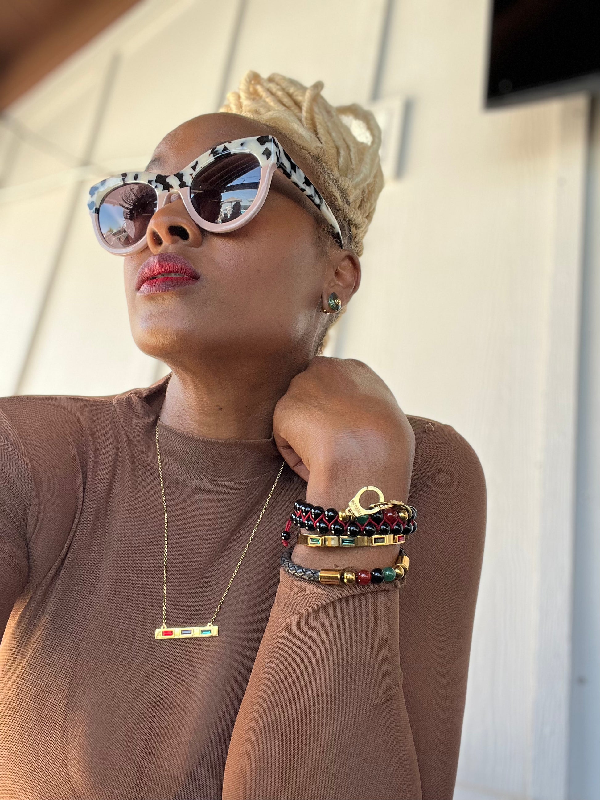 Person wearing sunglasses and a brown top with colorful bracelets on a neutral background