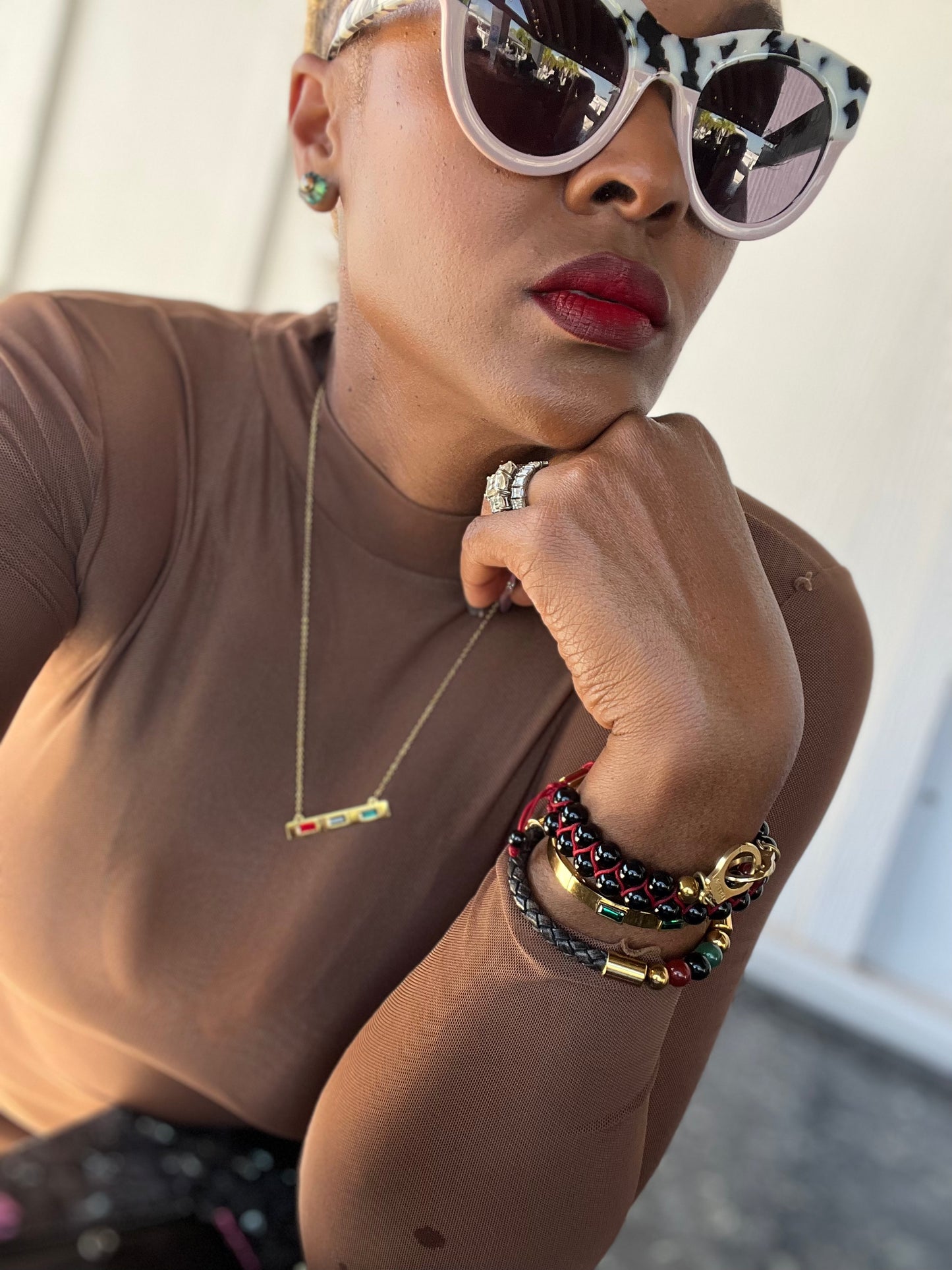 Person wearing sunglasses, a necklace, and multiple bracelets with a neutral background